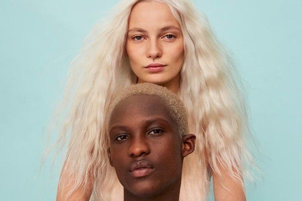 Hairshop Pro: Studio-Kampagne mit zwei Models – platinblondes Langhaar und kurzer aschblonder Buzzcut vor hellblauem Hintergrund