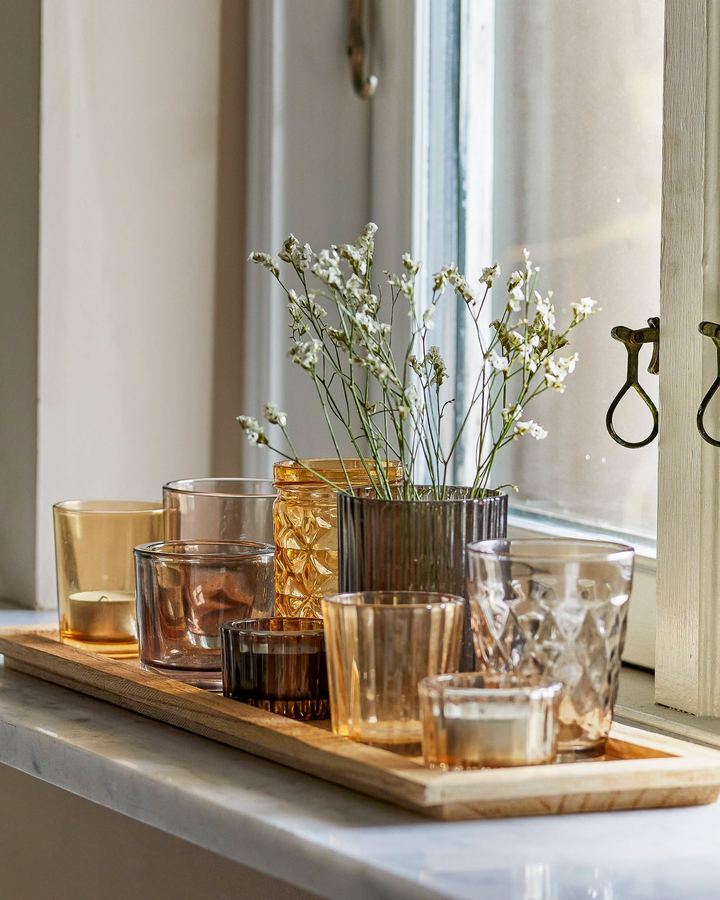 Coloured glasses and tealight holders on a wooden tray by the window