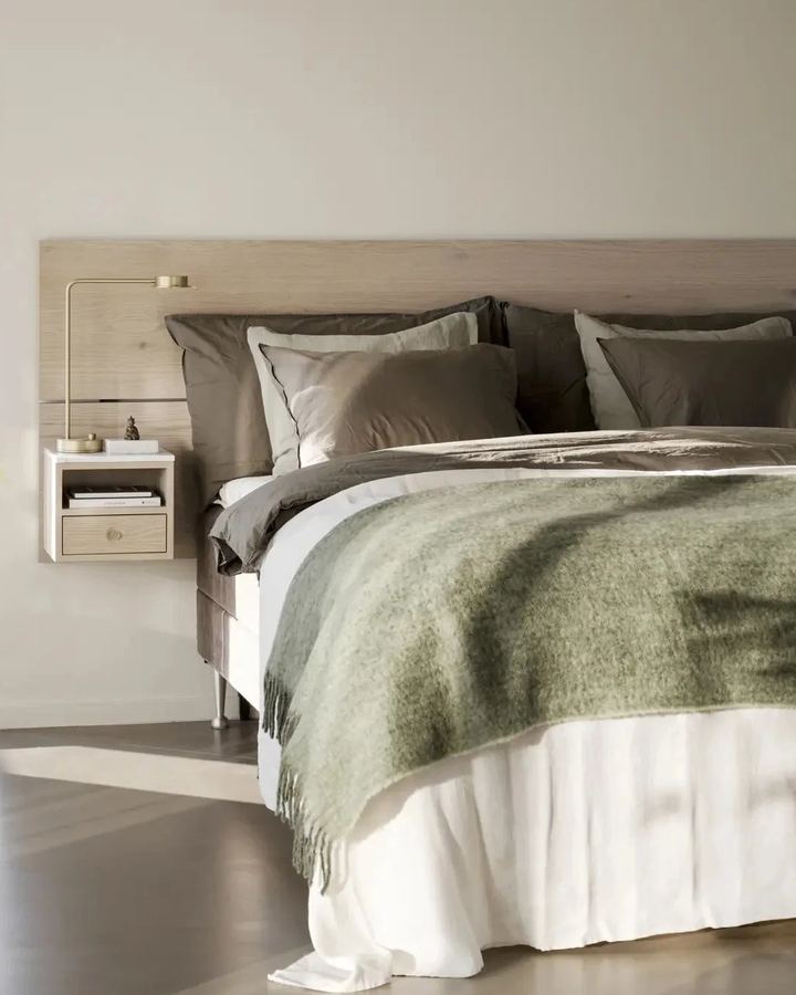 Schlafzimmer mit Leinenbettwäsche, grüner Wolldecke und Wandkonsole