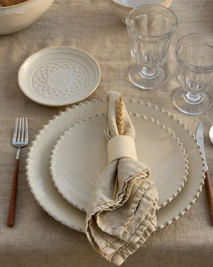 Gedeckter Tisch mit Perlrand-Tellern, Leinenserviette und Gläsern auf Leinen