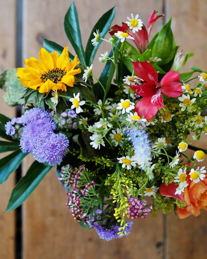 Bunter Wiesenstrauss mit Sonnenblume, Kamille und Alstroemerien vor einer Holzwand