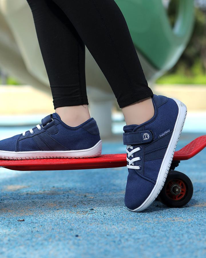 Kind steht mit Freiluftkind-Kinderbarfußschuhen auf einem Skateboard auf dem Spielplatz