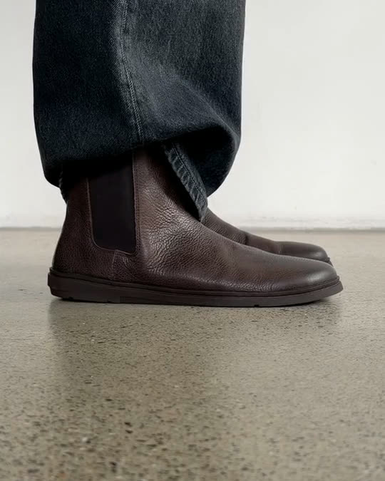 Brown leather Groundies Chelsea boots stepping into frame on a concrete floor
