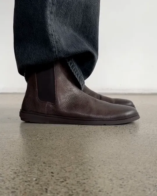 Brown leather Groundies Chelsea boots stepping into frame on a concrete floor