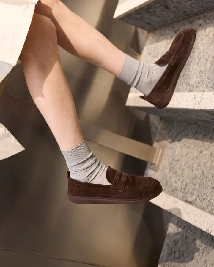 Beine in grauen Socken und braunen Wildleder-Loafern auf einer Betontreppe