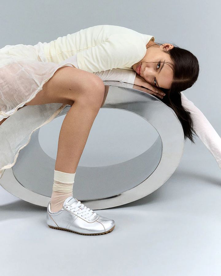 Frau lehnt im Studio auf einer Metallskulptur, silberne Groundies-Sneaker