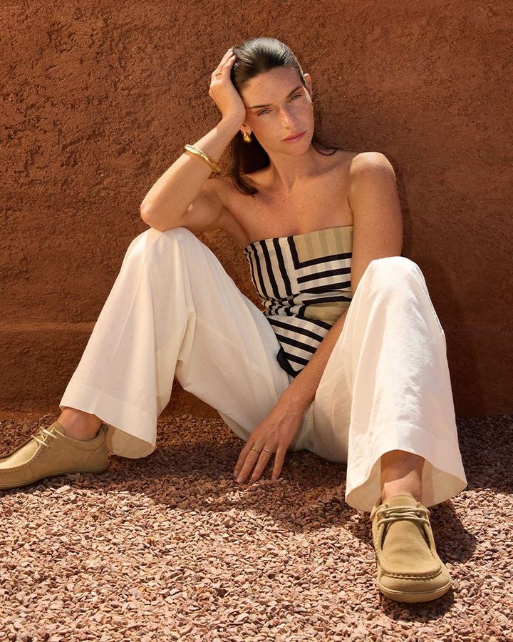 Woman sitting against a terracotta wall on gravel, wearing Groundies shoes