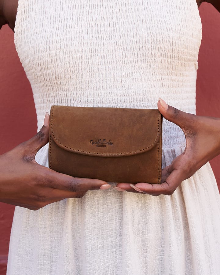 Hands holding a brown leather clutch in front of a white summer dress