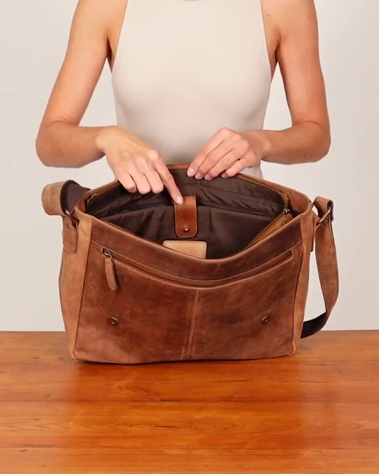 Hands opening a brown leather Gusti messenger bag and showing the inner compartments