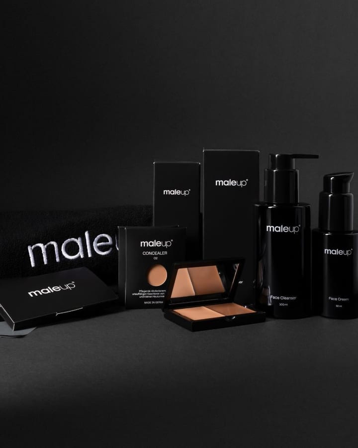 Schwarze maleup-Produkte mit Concealer-Palette, Spendern und Handtuch vor dunklem Hintergrund