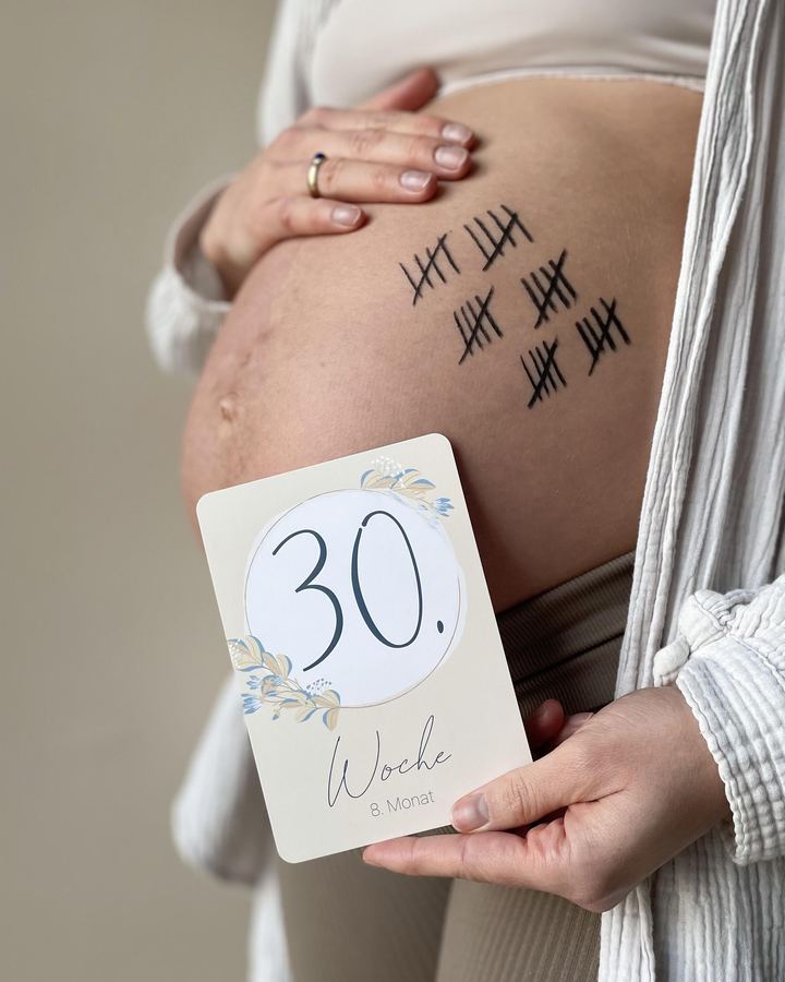 Schwangere hält eine Mintkind-Wochenkarte „30. Woche“ an den Bauch