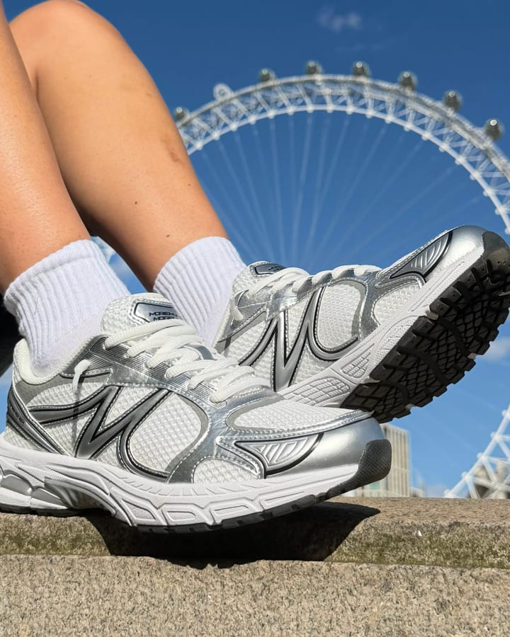 Silver and white sneakers with white socks on a wall, a Ferris wheel against a blue sky in the background