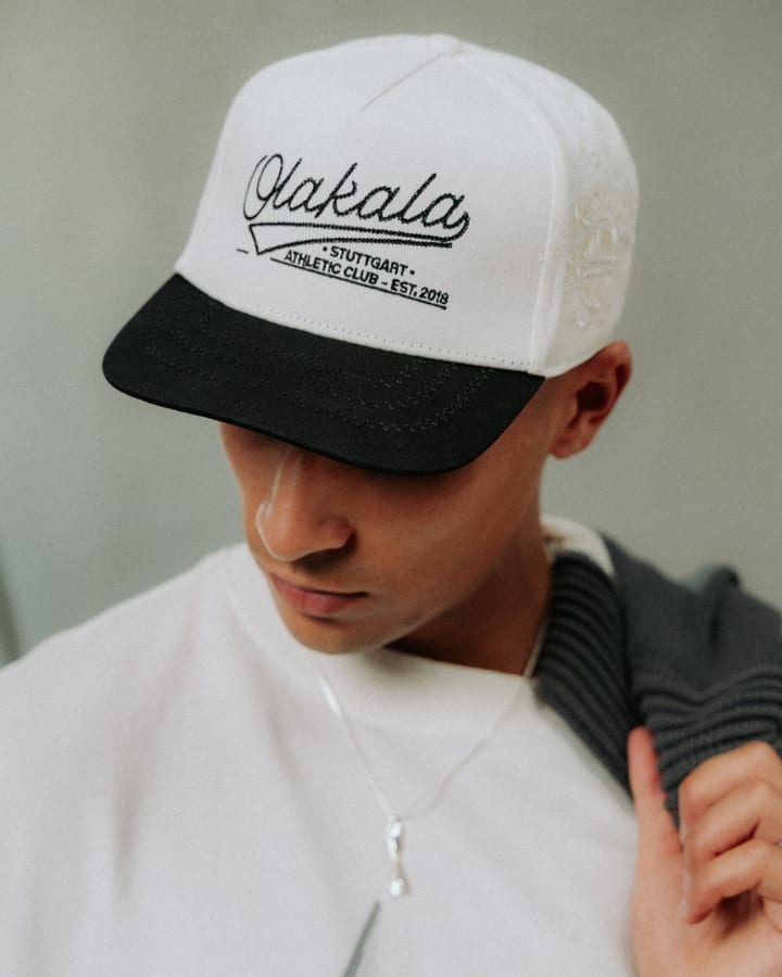 Mann mit gesenktem Blick trägt eine weisse Olakala-Cap mit schwarzem Schirm und weisses T-Shirt