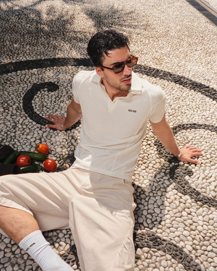 Man in sunglasses wearing a cream polo and shorts sitting on a pebble mosaic