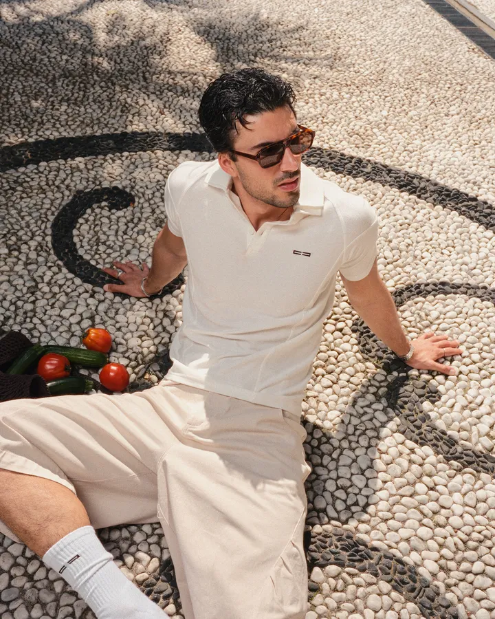 Man in sunglasses wearing a cream polo and shorts sitting on a pebble mosaic