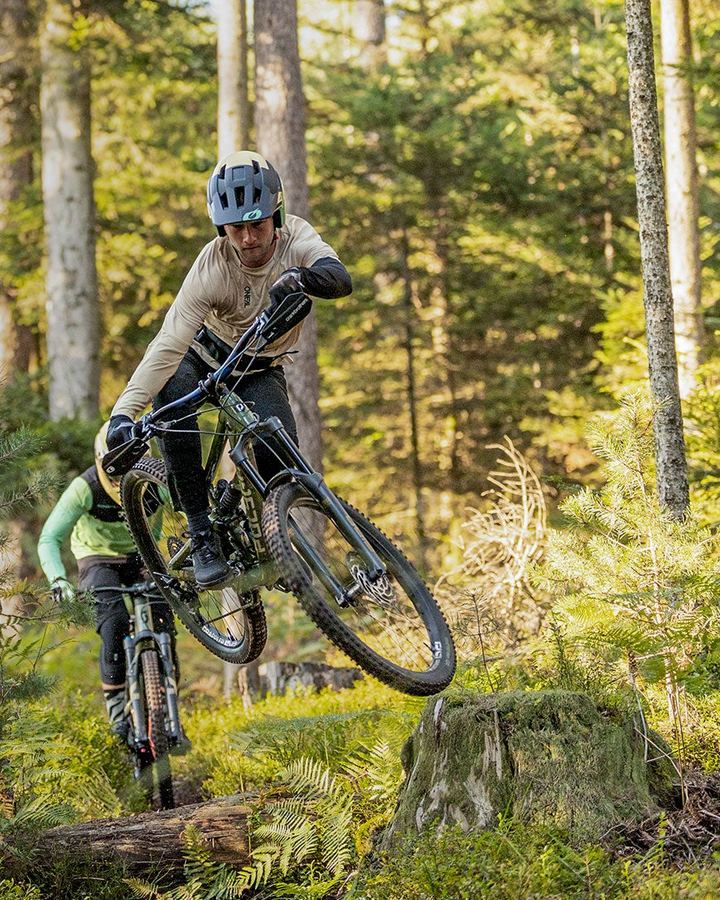Two mountain bikers jumping a ledge in the forest