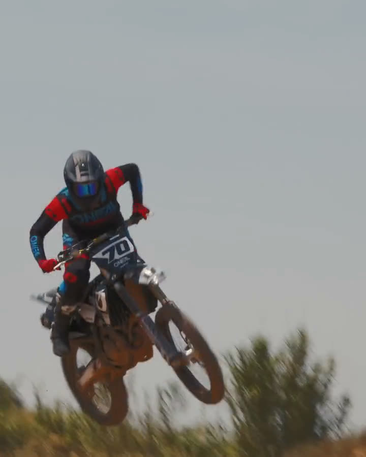 Motocross-Fahrer mit O'Neal-Brille und Helm, danach im Sprung über eine Kuppe