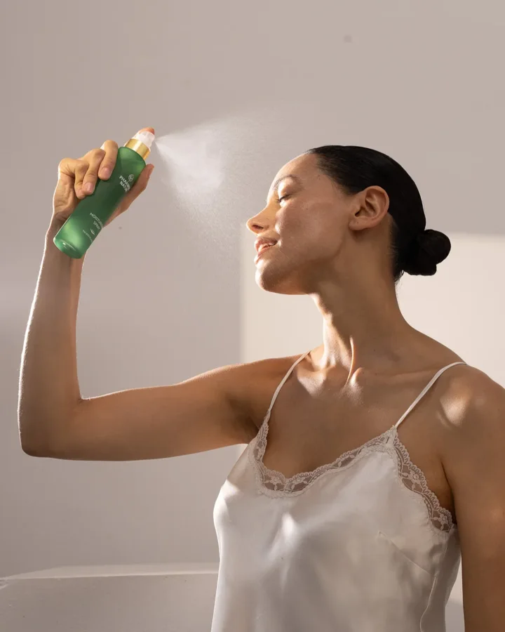 Frau trägt PHARMOS NATUR Gesichtsspray im warmen Sonnenlicht auf.