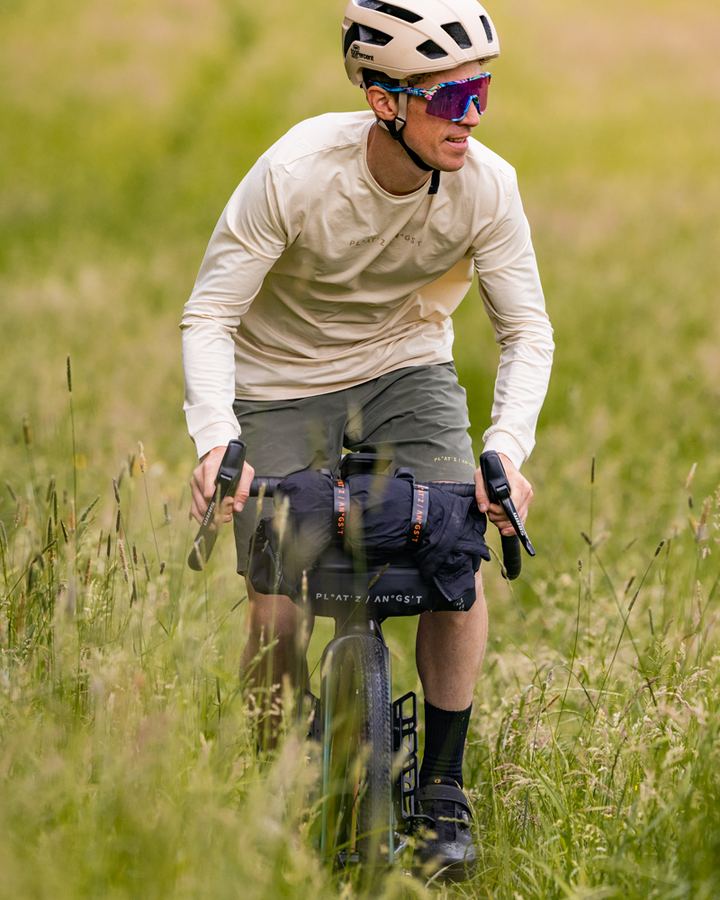 Gravel rider with a handlebar bag riding through tall grass