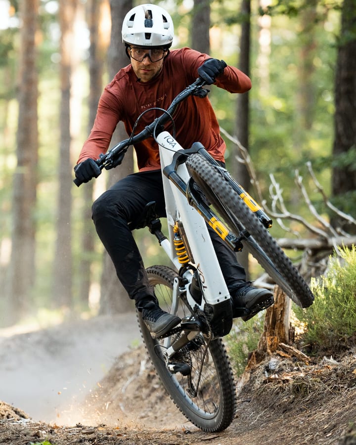 Mountain biker in a red long-sleeve jersey and white helmet riding through the forest with the front wheel lifted