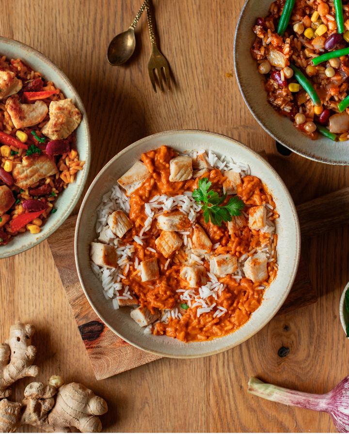 Three meal bowls with chicken, rice and vegetables on a wooden table, top view