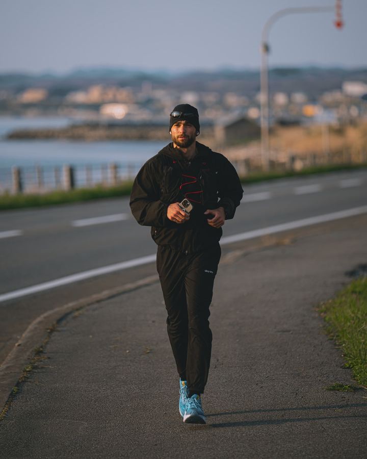 Läufer in dunkler Sportkleidung auf einem Uferweg in der Abendstimmung