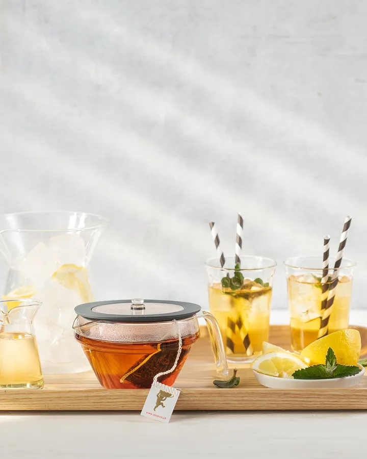 Glass teapot, a carafe of ice cubes and two glasses of iced tea with mint on a wooden tray