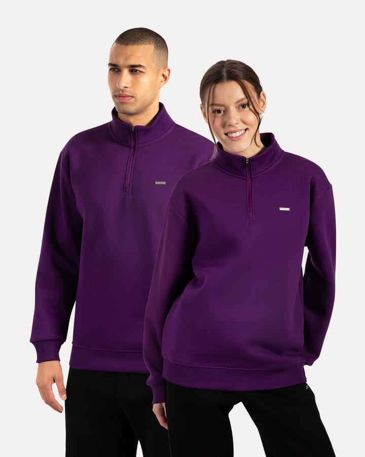 Man and woman in purple half-zip sweatshirts standing against a light studio background