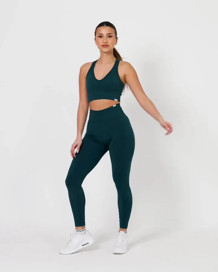 Model dreht sich im dunkelgrünen SMILODOX-Set aus Bustier und Leggings vor weißem Hintergrund