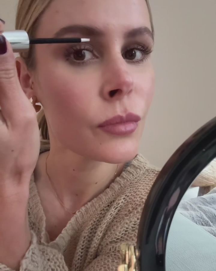 Frau trägt vor einem Schminkspiegel Wimperntusche auf.