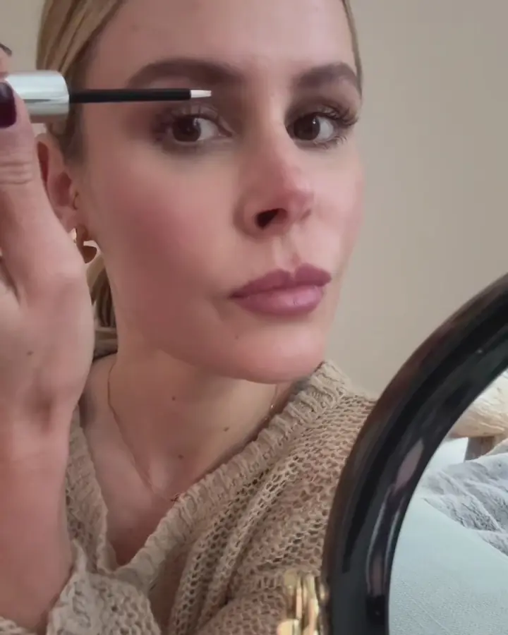 Woman applying mascara in front of a vanity mirror.